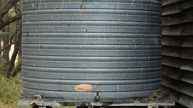 Cuve de récupération d'eau de pluie en métal galvanisé installée au pied d'une cabane, alimentée par la gouttière du toit.