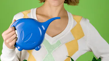 Femme arrosant ses plantes d'intérieur avec un arrosoir bleu avant absence.