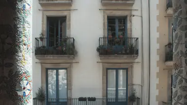 Façade méditerranéenne avec plantes en pot sur balcon en fer forgé, feuillage vert et plantes en jardinières typiques du sud.