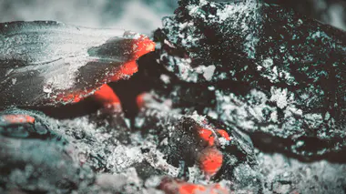 Cendres de bois grises et braises dans un foyer, résidu de combustion à valoriser au jardin avec modération